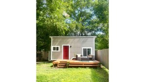 A small, single-story house with a red door, a deck, and a fenced backyard. - 🏡Cozy Farmhouse Tiny Home in Backyard Pool Oasis🌻 (Austin)