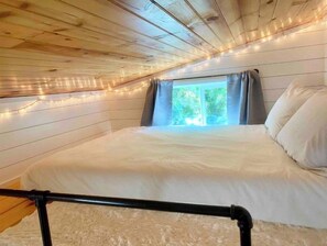A bedroom with a wooden ceiling, a bed with white bedding, and a window with curtains.