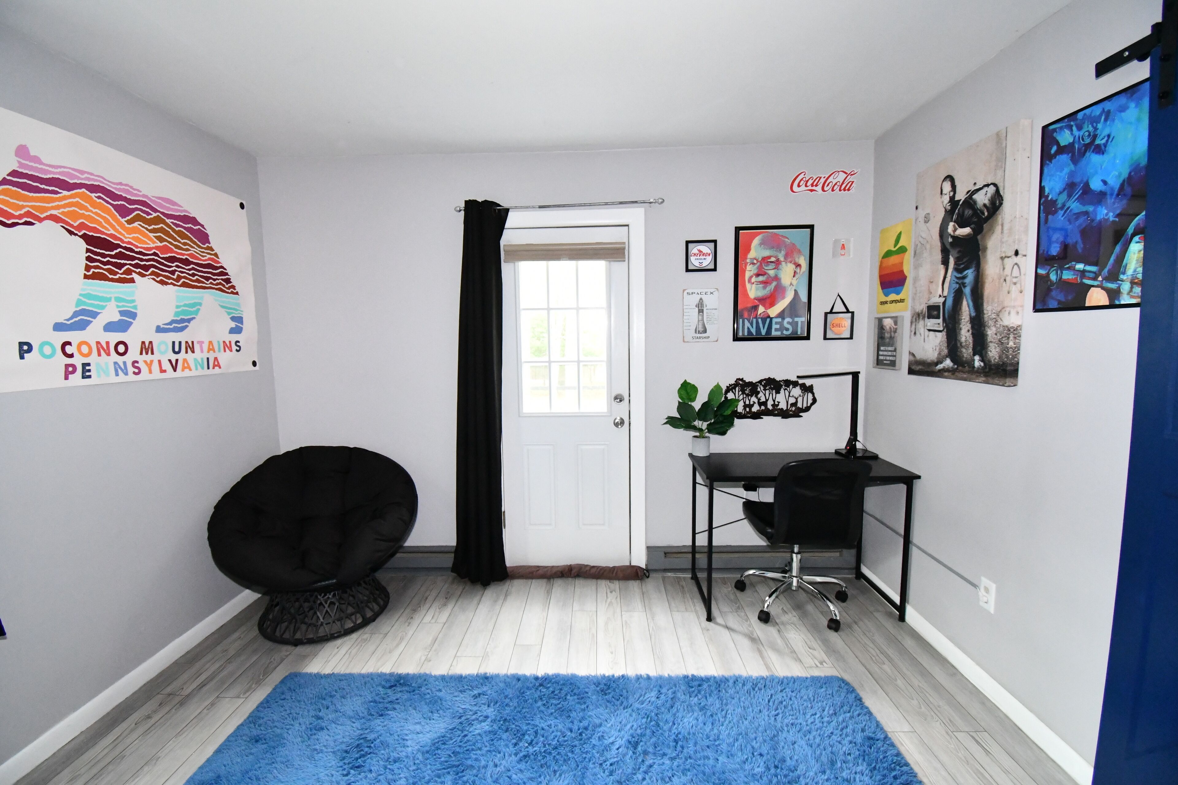 Une chambre moderne avec une porte blanche, un fauteuil en forme de sac de haricots noir, un bureau avec un ordinateur et un tapis bleu.