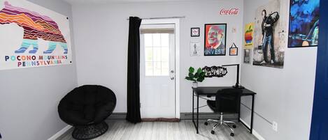 Une chambre moderne avec une porte blanche, un fauteuil en forme de sac de haricots noir, un bureau avec un ordinateur et un tapis bleu.