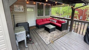 A covered outdoor seating area with a red sofa, a small table, and string lights.