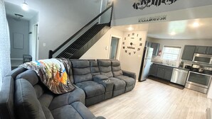 A modern living room with a sectional sofa, a staircase, and a kitchen area.