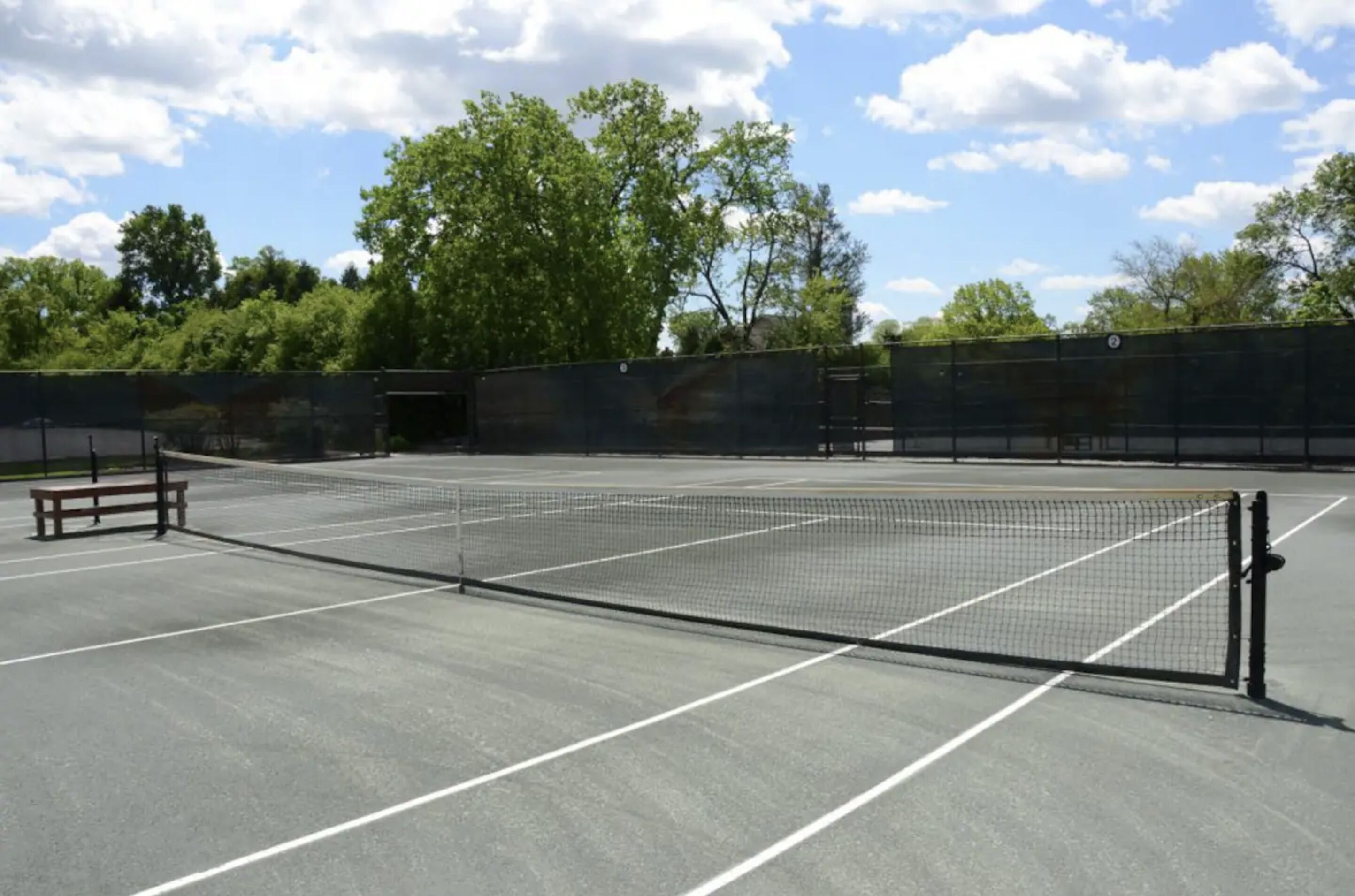 Ein Tennisplatz im Freien mit Netz, Bänken und einer Umzäunung.