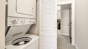 Pesutila, jossa on etuaukollinen pesukone ja kuivausrumpu, valkoinen ovi ja käytävä, joka johtaa toiseen huoneeseen.