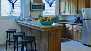 A kitchen with wooden cabinets, a stainless steel refrigerator, a fruit bowl on the counter, and a microwave above it.