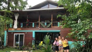 A two-story house with a balcony, surrounded by lush greenery and several surfboards.