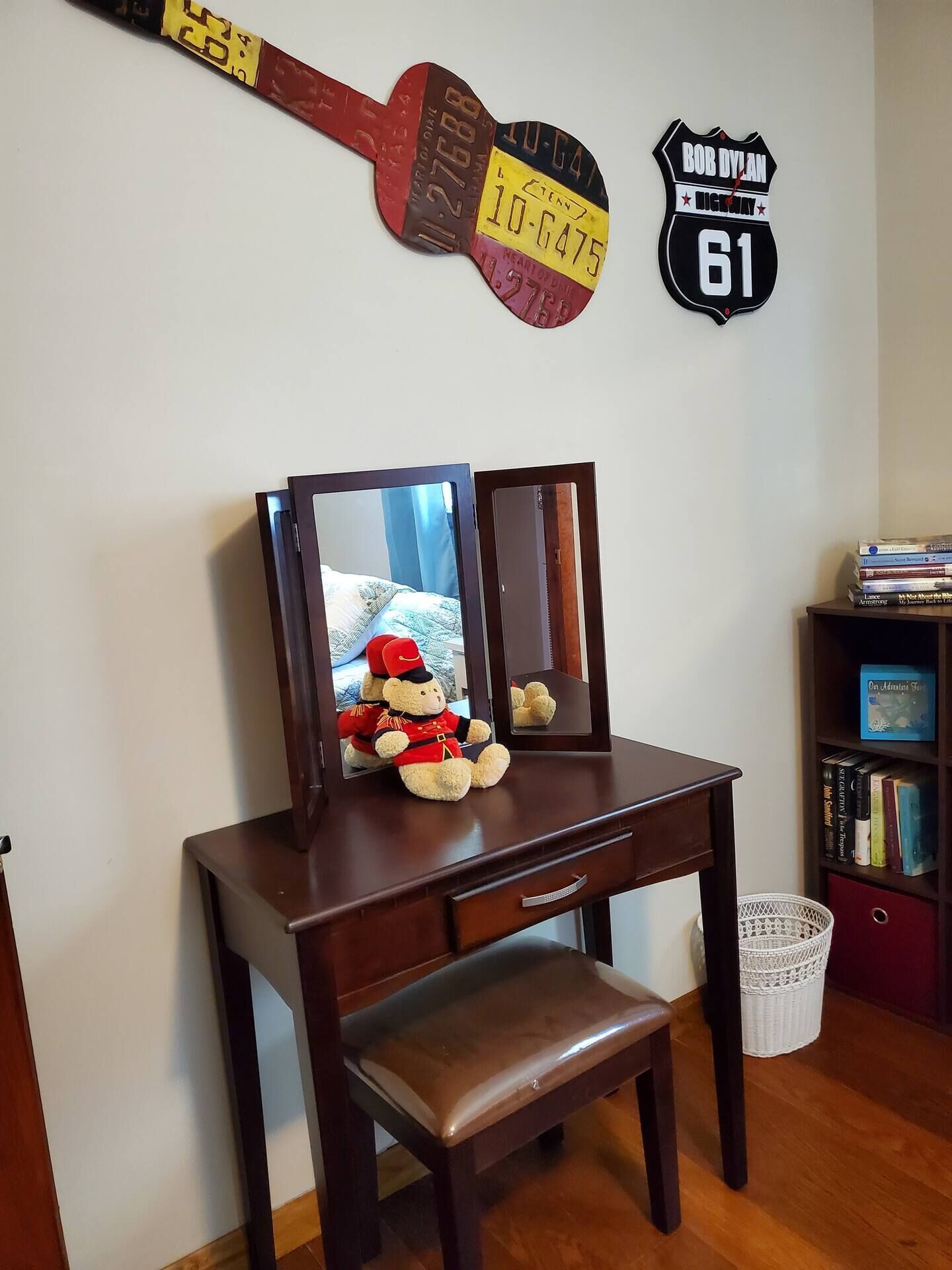 A wooden desk with a mirror, a teddy bear, and a guitar-shaped sign on the wall.
