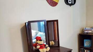 A wooden desk with a mirror, a teddy bear, and a guitar-shaped sign on the wall.