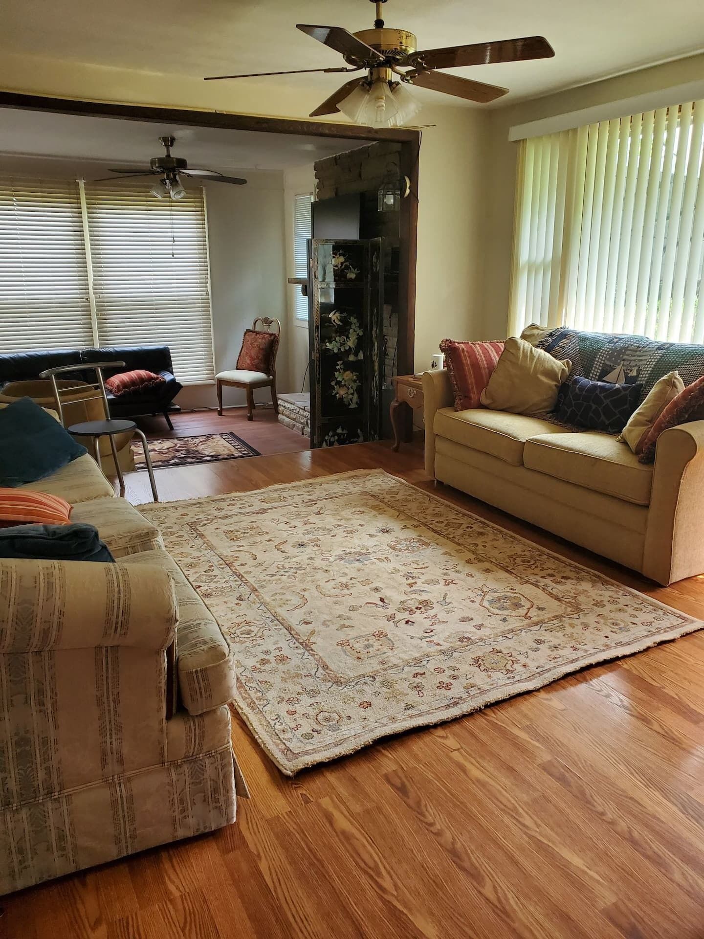 Una sala de estar con piso de madera, un sofá color beige, un tapete estampado y un ventilador de techo.