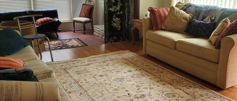 Una sala de estar con piso de madera, un sofá color beige, un tapete estampado y un ventilador de techo.
