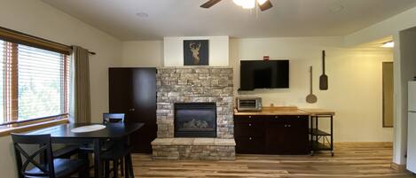 A living room with a stone fireplace, a ceiling fan, a flat-screen TV, and a dining area with wooden flooring.