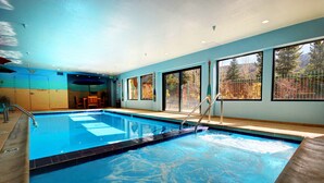 An indoor swimming pool with clear blue water, surrounded by large windows offering views of trees and mountains. - Gateway Lodge 5037 (Keystone)