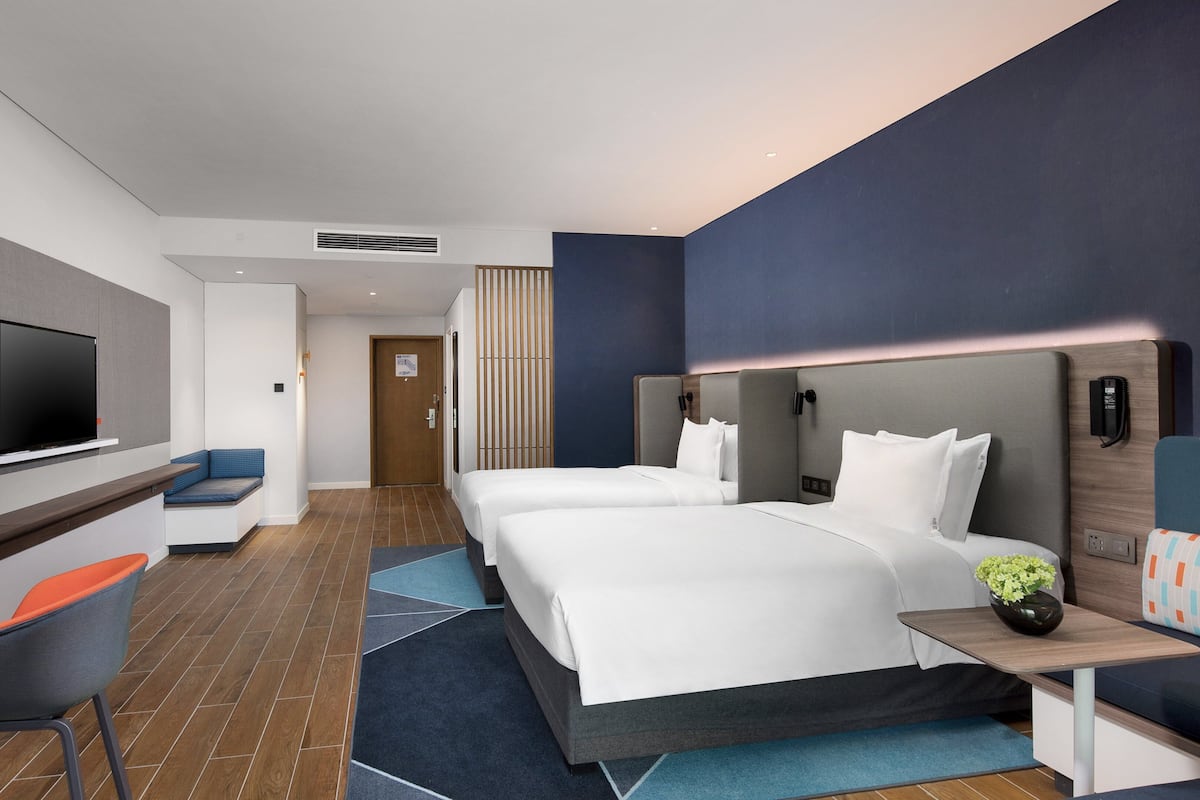 A modern hotel room with two beds, a TV, a desk, and a seating area.