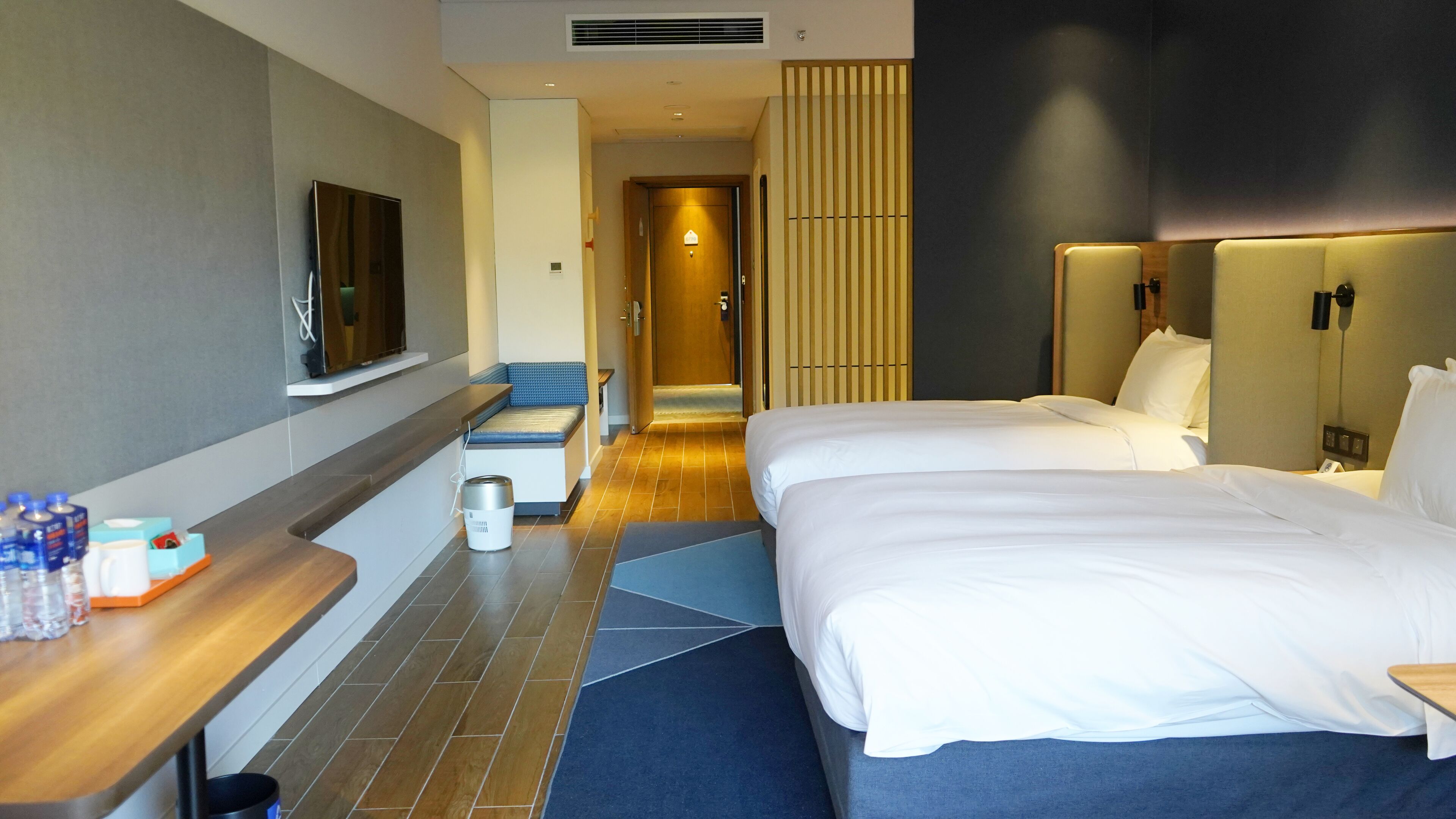A hotel room with two beds, a desk, a TV, and a bathroom.