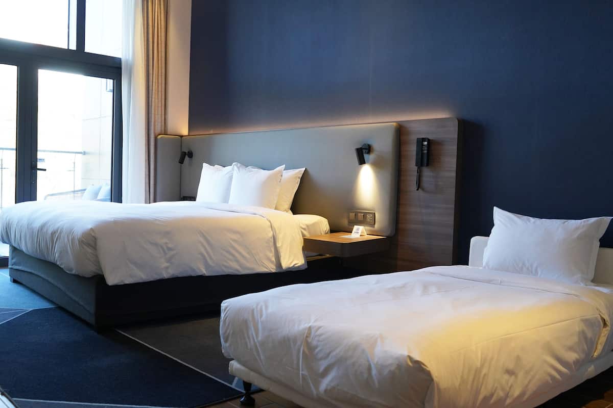 A hotel room with two beds, a large window, and a phone on the wall.