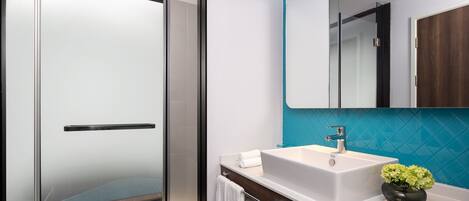 A modern bathroom with a glass shower door, a white sink with a mirror above it, and a teal accent wall.