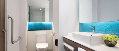 A modern bathroom with a white toilet, a sink with a mirror, and a blue-tiled shower area.