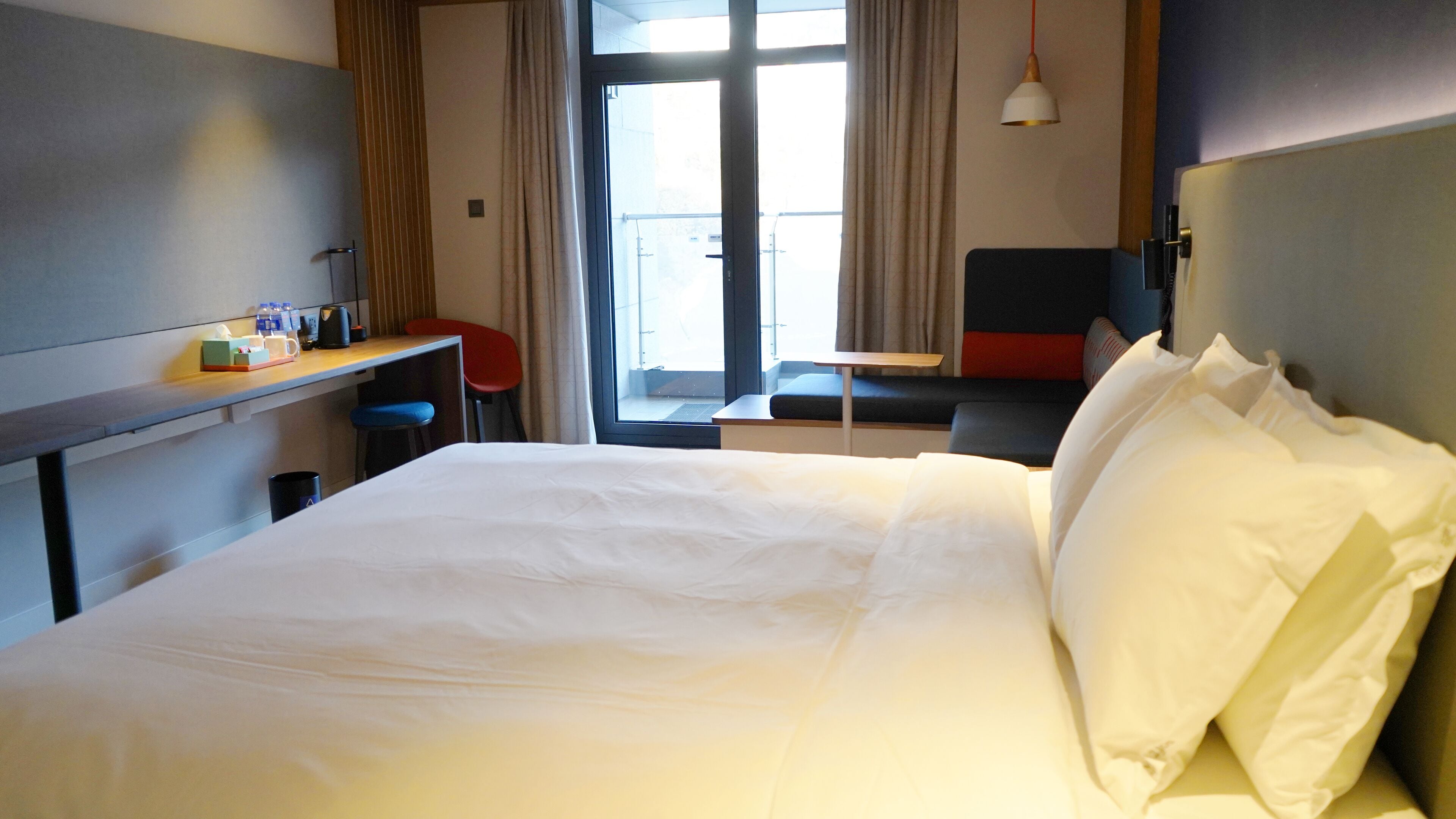 A hotel room with a bed, a desk, a chair, a table, and a window with curtains.