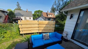 An outdoor patio area with a blue sofa set, a wooden fence, and a small table.