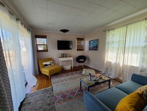 Een woonkamer met een gele fauteuil, een blauwe bank, een kamerbreed tapijt met een patroon, een klein wit tafeltje en een televisie bevestigd aan een bakstenen muur.
