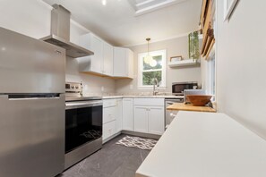 Een moderne keuken met roestvrijstalen apparatuur, witte kasten en een raam met uitzicht op groen.