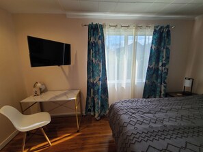 A bedroom with a bed, a desk, a chair, a TV, and curtains.