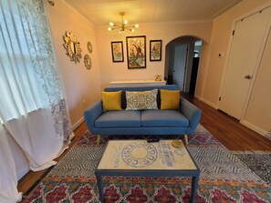 Una sala de estar con un sofá azul, cojines amarillos, un tapete estampado y una mesa de centro de diseño vintage.