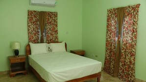 Un dormitorio con cama, mesitas de noche, una lámpara y cortinas con motivos florales.
