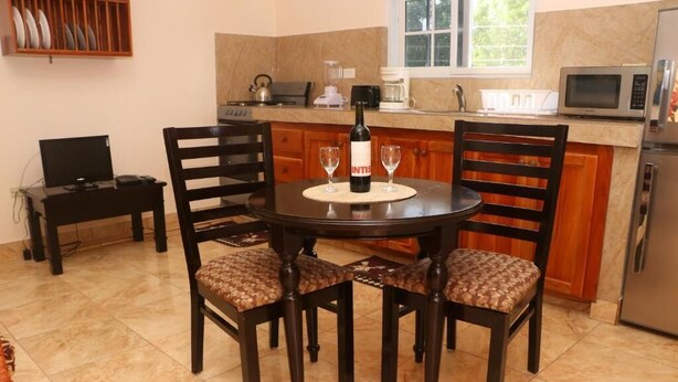 Un comedor con una mesa redonda, cuatro sillas, una botella de vino y dos copas sobre un mantel individual.