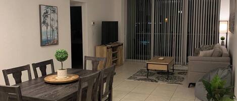 A dining area with a wooden table and chairs, a small plant on the table, and a ceiling light.