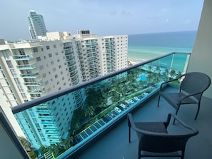 Un balcon avec vue sur une piscine, des palmiers et des immeubles de grande hauteur.