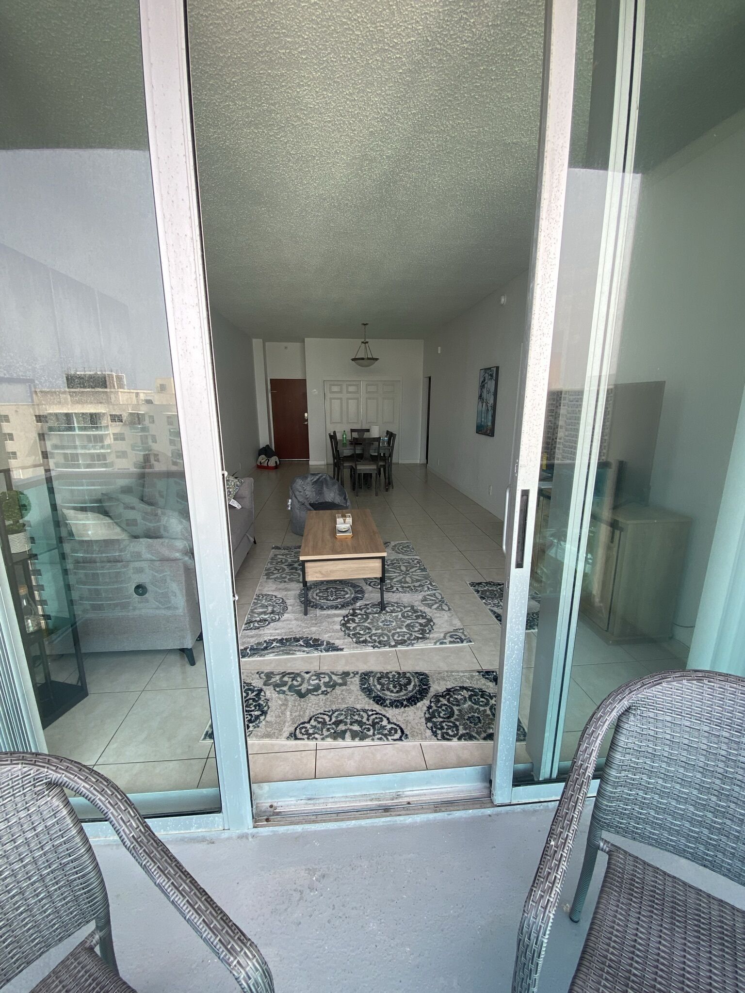 A view from a balcony into a living area with a dining table, chairs, and a patterned rug.