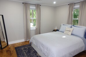 Une chambre à coucher avec un lit, une table de chevet, un miroir et une fenêtre avec des rideaux.