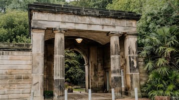 A stone archway with columns, surrounded by greenery and a paved entrance.