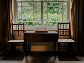 Una habitación con ventana, dos sillas de madera, una mesa y un tablero de ajedrez.