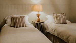 Deux lits simples avec des oreillers à rayures, une petite table avec une lampe et une tête de lit en bois.