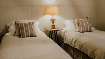 Two single beds with striped pillows, a small table with a lamp, and a wooden headboard.