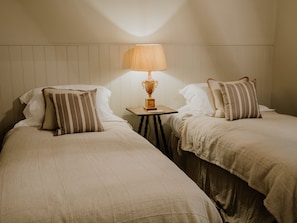Dos camas individuales con almohadas a rayas, una mesita con una lámpara y un cabecero de madera.