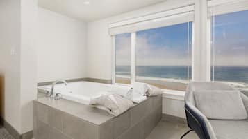 A bathroom with a large bathtub, a window with a view of the ocean, and a chair.