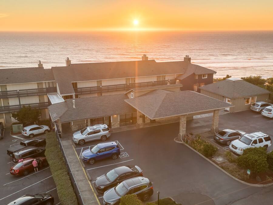 A hotel with a parking lot and a view of the ocean at sunset.