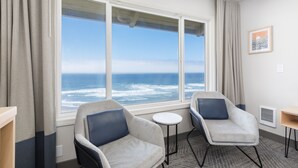 A room with two armchairs, a small table, and a large window with a view of the ocean. - Surfland Hotel (Lincoln City)