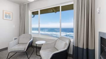 A room with two armchairs, a small table, and a large window with a view of the ocean.