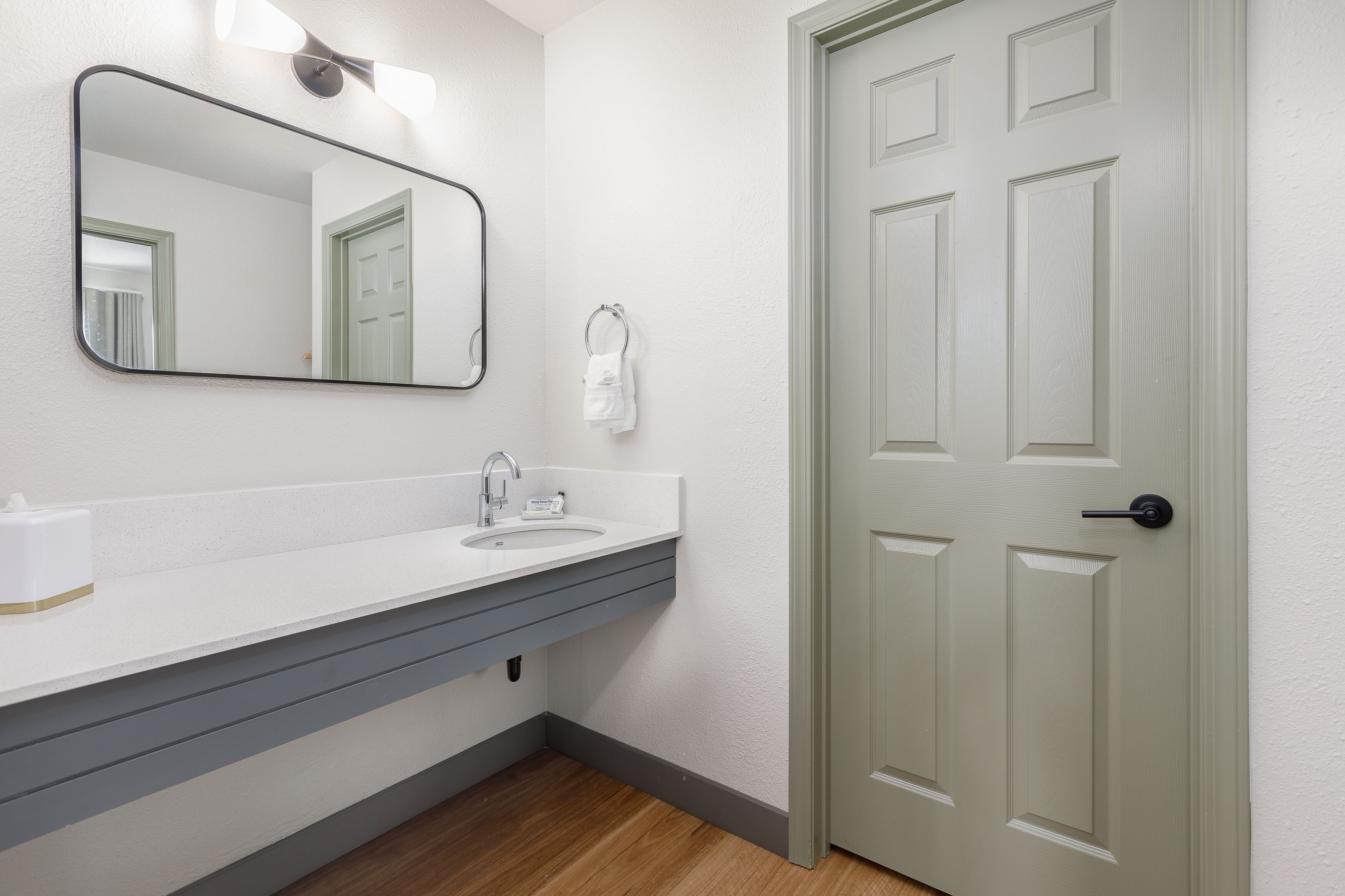 Un baño con lavamanos blanco, espejo y puerta con manija.
