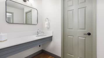Un baño con lavamanos blanco, espejo y puerta con manija.