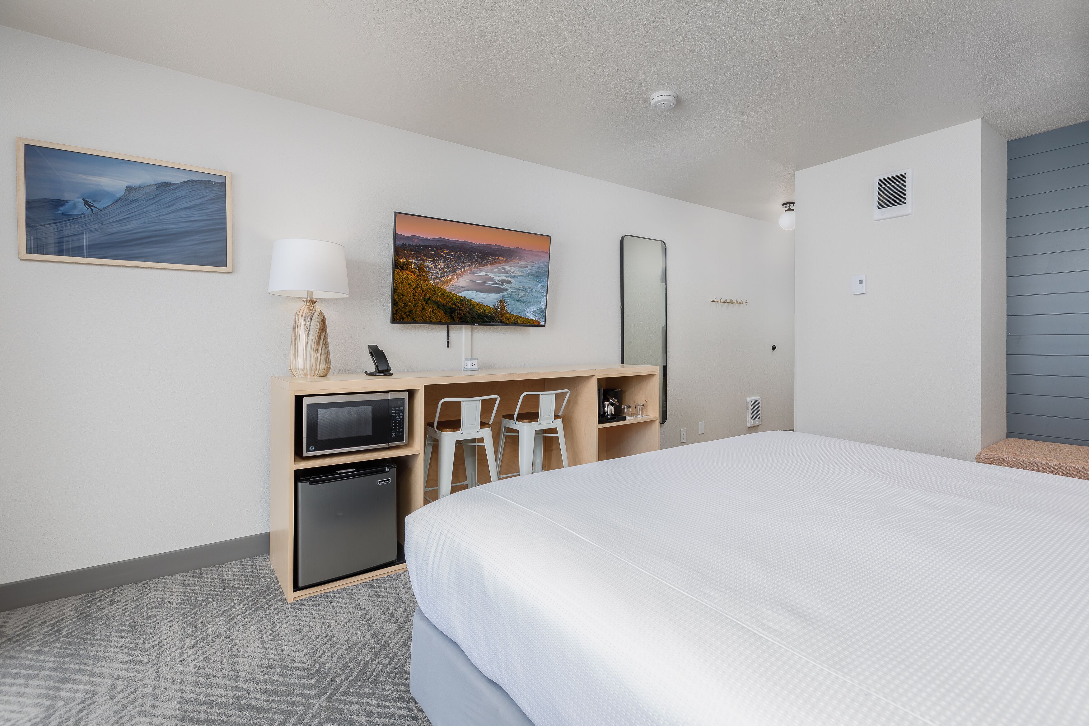 A hotel room with a bed, a desk with a computer, a TV, and a small fridge.