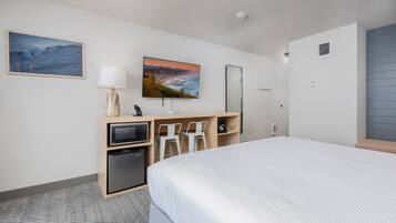 Una habitación de hotel con cama, escritorio, computadora, televisión y un refrigerador pequeño.