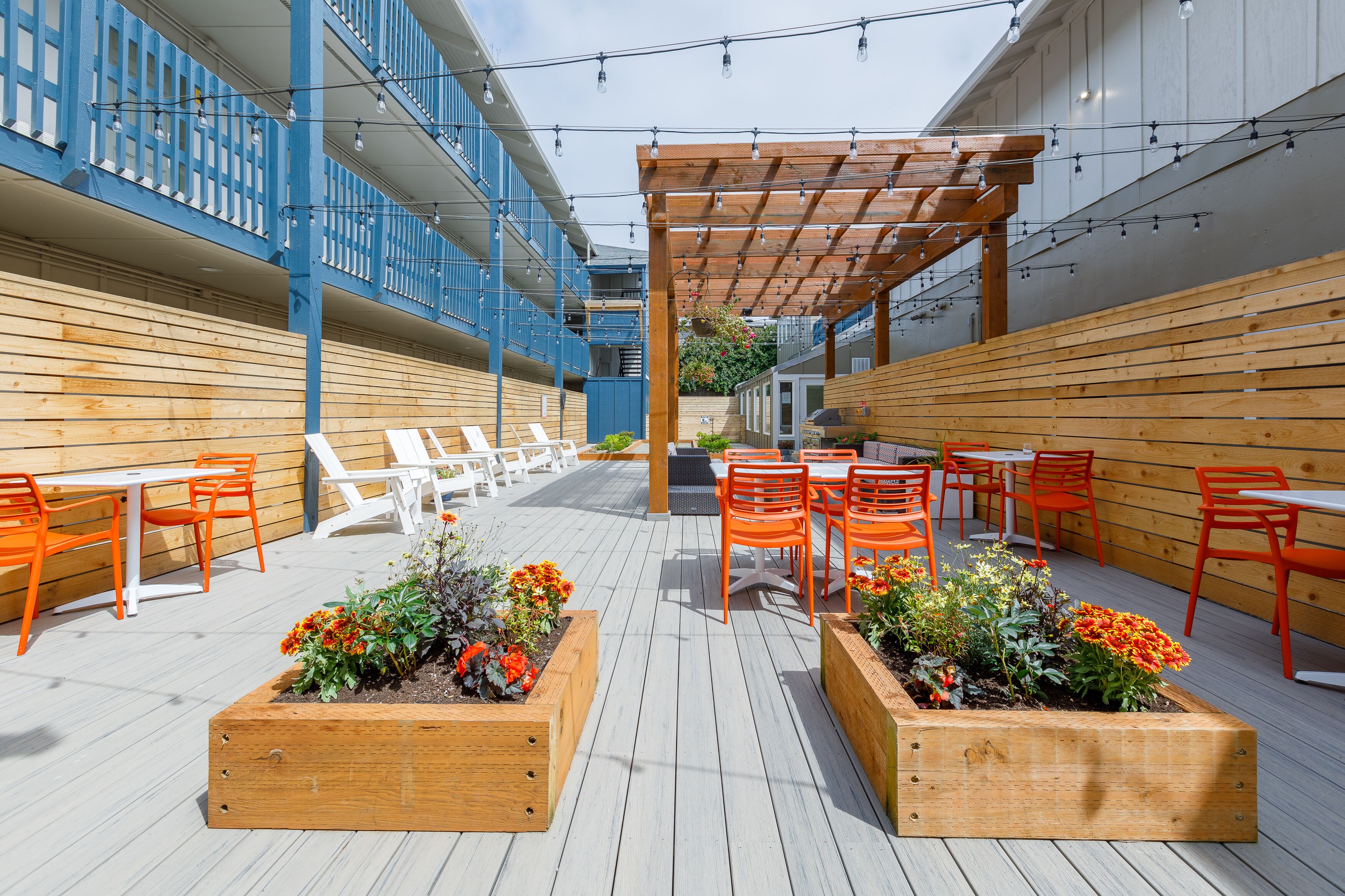 An outdoor patio with wooden planters, orange chairs, and tables.
