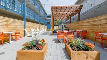 An outdoor patio with wooden planters, orange chairs, and tables.