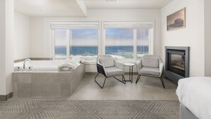 A modern bathroom with a bathtub, two chairs, a small table, and a fireplace. - Surfland Hotel (Lincoln City)