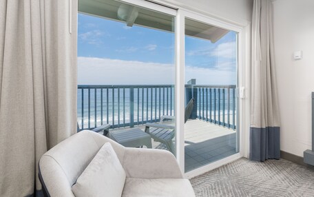 A balcony with a view of the ocean, a white chair, and a glass door.
